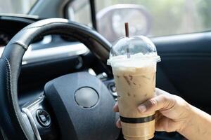 woman driver hold ice coffee cup for drink in car, dangerous accident. photo