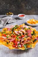 Charcuterie nachos with chips, salami, cheese and olives on a plate on a table vertical view photo