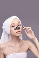 Young caucasian female applying charcoal face mask for blackhead removal and skincare routine. photo