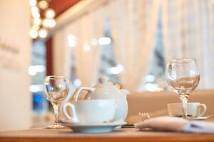 Elegant table setting with white teapot and glassware in cozy cafe ambiance. photo