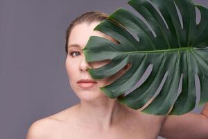 Caucasian adult female with monstera leaf against gray background in artistic minimalist portrait. photo