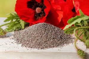 Poppy seeds and poppy flowers on a wooden background photo