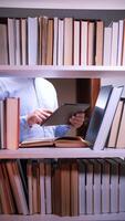 A man is using a tablet computer in front of a shelf full of books video