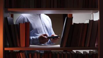 A man holding a cell phone in front of a book shelf video