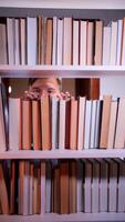 A man peeking out from behind a book shelf video