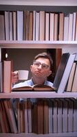 A man in glasses is looking at a book shelf with a cup of coffee video