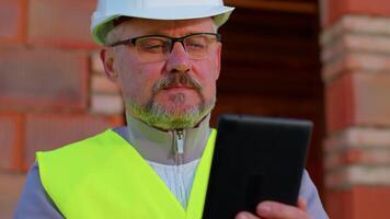Male construction engineer. Architect with a digital tablet computer at construction site. Man worker foreman looking analyzing blueprints, building house place on background. Construction concept. video