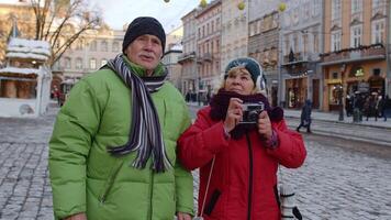 mayor esposa y marido turistas tomando foto imágenes en retro cámara, caminando, gesticulando en invierno ciudad calle en lviv, Ucrania. familia vacaciones ocupaciones y fotografía. vida después Jubilación. video