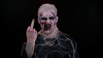 Aggressive crazy hooligan Halloween zombie man with makeup with wounds scars showing around his middle fingers, demonstrating protest with impolite rude gesture of disrespect, rejecting communication. video