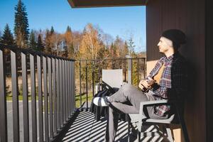 Musician sits on a sunny balcony, immersed in playing the ukulele. Surrounded by autumn trees, he enjoys the peaceful moment outdoors, lost in his thoughts and music photo