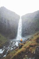 Tourist stands in awe before Grundarfoss waterfall on the Snaefellsnes Peninsula, Iceland, as mist rises from the cascading water against rugged basalt cliffs photo