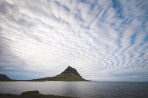 Kirkjufell mountain on the Snafellsnes Peninsula in west Iceland, stands majestically with its reflection mirrored in the still waters below, under a soft, pastel sky photo
