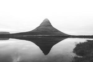 Black and white Kirkjufell, the iconic mountain on the Snafellsnes Peninsula in west Iceland, stands majestically with its reflection mirrored in the still waters below photo