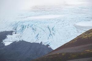 Close-up view of a stunning Icelandic glacier flowing between dark volcanic slopes and mossy ridges. A raw contrast of ice and earth in the heart of Snaefellsnes Peninsula photo