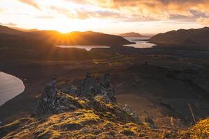Adventurer climbs on the end of The Horn mountain on Snaefellsnes peninsula in Iceland as golden light from the setting sun illuminates the rugged volcanic terrain below. Stand on the edge photo