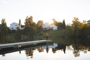 Man enjoys on pier an Oslo lake, Holmendammen as the sun sets behind charming houses, capturing a peaceful moment of reflection and stillness in Norway autumn magic photo