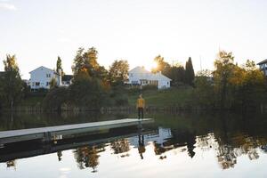 Man walks on pier an Oslo lake, Holmendammen as the sun sets behind charming houses, capturing a peaceful moment of reflection and stillness in Norway autumn magic photo