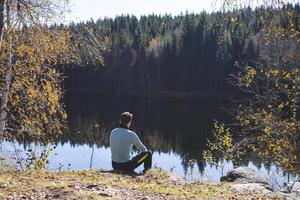 Man rests by the forest lake in Oslo Marka, soaking in the quiet beauty of nature and reflecting in the stillness of the Norwegian wilderness photo