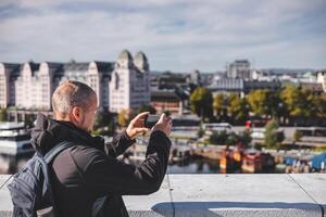 Capturing Oslo from Opera house, a Man frames the city through his phone. Old man is using modern technology. Taking a pictures photo