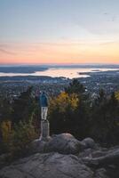 High above Oslo, a lone soul balances on stone, surrounded by golden trees and fading daylight, where forest stillness meets the endless horizon of the fjord photo