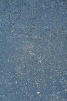 Dark speckled asphalt texture with a small leaf fragment, creating a unique surface pattern photo
