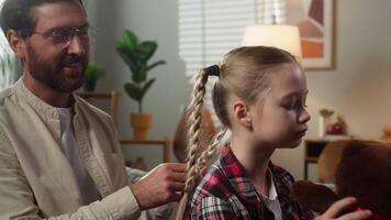 Happy family at home couch pretty daughter child kid girl playing with teddy bear loving father making pigtails braids dad helping with long hair hairdo care talking bonding custody adoption childcare video