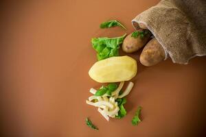 Root vegetable in a sack and sliced potatoes on a brown background photo