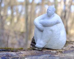 A plaster sculpture of a curvy, dreamy woman sitting on the trunk of a fallen tree, surrounded by the soft whispers of a blooming spring park photo