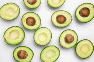 Halved avocados with and without pits arranged on a plain white surface in a top down view shot photo