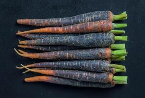 A close up shot of a stack of purple carrots with green stems against a black background surface photo
