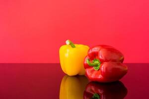 A still life of a yellow and red bell pepper on a reflective surface against a red background photo