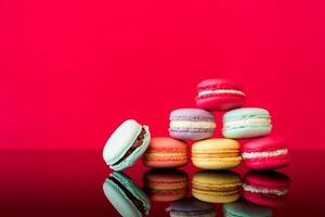 A stack of colorful macarons on a reflective surface with a bright red background in a studio shot photo
