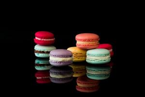 A studio shot of colorful macarons stacked on a reflective black surface with a dark background photo