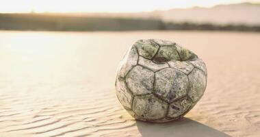 CGI Old soccer ball rests on sandy beach during sunset video