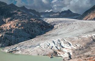 Aerial view of a glacier flowing into a lake surrounded by mountains under a cloudy sky landscape photo