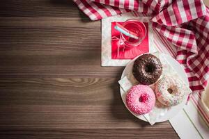 Overhead view of donuts and a drink on a wooden table with checkered and striped cloths around it photo