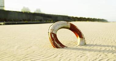 CGI Lifebuoy rests on sandy beach with urban structures in background video