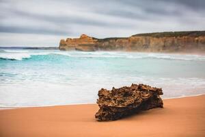 A rock formation on a sandy beach with ocean waves and cliffs in the distant background view scene photo
