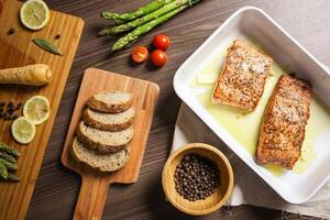 Overhead shot of salmon fillets with asparagus, bread, and tomatoes on a wooden table surface photo