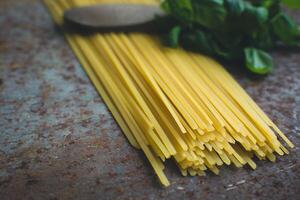 Close up of uncooked spaghetti with basil leaves on a textured surface in a kitchen setting photo