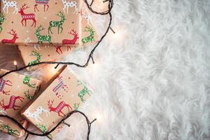 Christmas presents with reindeer wrapping paper and lights on a fluffy white background in a top view photo