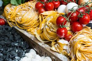 A vibrant display of fresh pasta varieties with tomatoes and mozzarella on a wooden surface top view photo