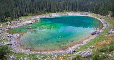 Aerial view of a turquoise lake surrounded by a dense forest on a bright day in the mountains photo