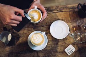 Person pouring milk into coffee cup creating latte art on a rustic wooden table surface view photo