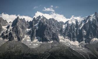 A view of jagged mountain peaks with snow and glaciers under a partly cloudy sky on a sunny day photo