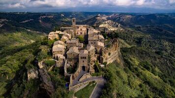 Aerial view of civita di bagnoregio perched on a cliff with surrounding green hills and cloudy sky above photo