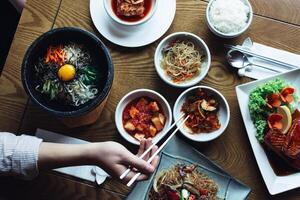 A top view of a table with korean dishes including bibimbap kimchi and japchae with chopsticks photo
