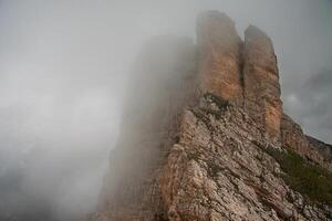 A rocky mountain peak shrouded in mist and low clouds on a cloudy day with limited visibility photo