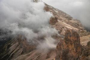 A view of rocky mountains covered in clouds with some snow patches on the peaks and slopes visible photo