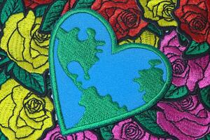 Handmade embroidery of a large heart with world map pattern, crafted from thread and fabric, placed on colorful rose-patterned textile. Eco-friendly concept for Earth Day and global warming awareness. photo